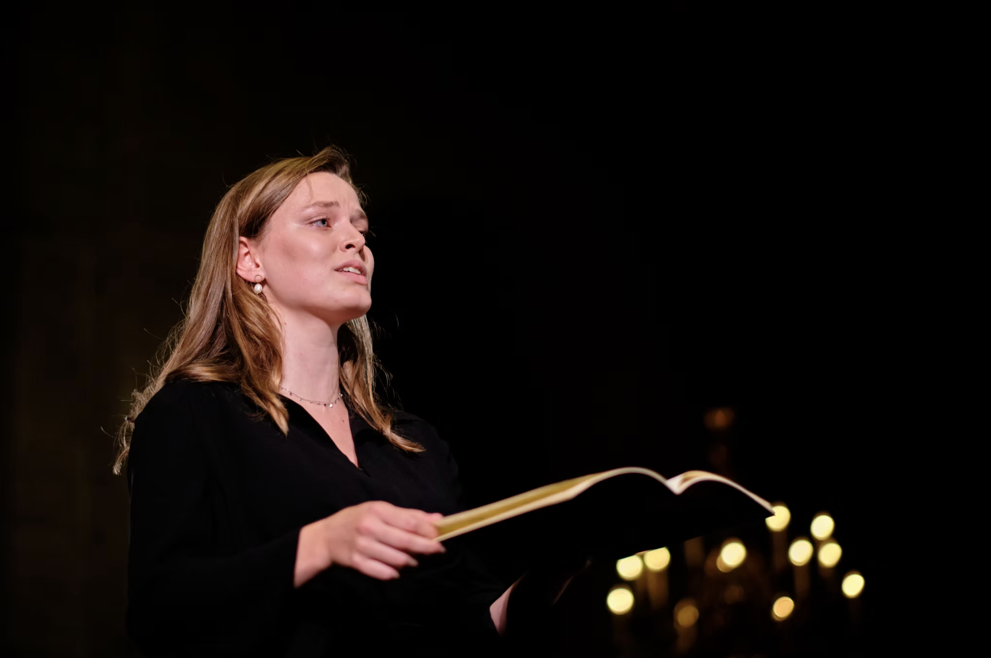 Nanette Mans zingt met bladmuziek in de hand, met kaarslicht op de achtergrond